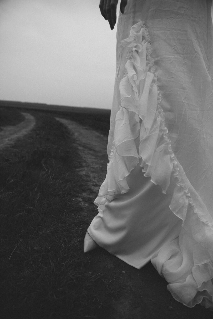 Black and white detail of a bride’s dress on a country road